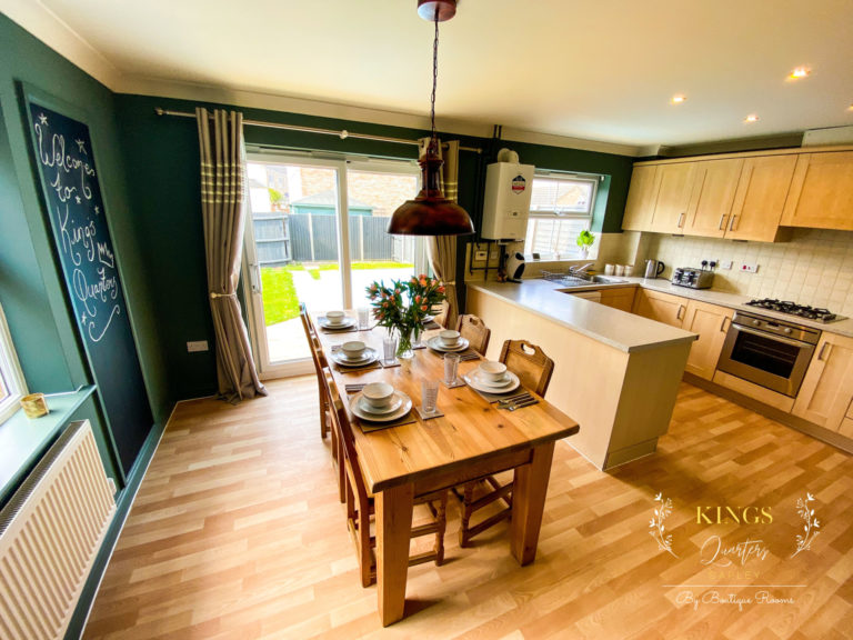 A green kitchen/diner with wood flooring and a wooden dining table set. Glass doors behind the table lead out to the garden.