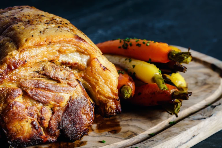 Close up of a piece of roast pork, next to it are some roasted carrots.
